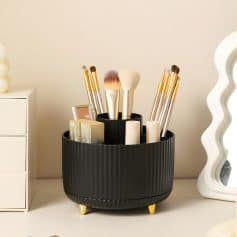 Elegant black makeup brush holder with gold-tipped brushes, skincare products, and a decorative mirror, showcasing beauty and skincare essentials on a sleek white vanity. perfect for professional and personal use.