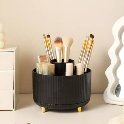Elegant black makeup brush holder with gold-tipped brushes, skincare products, and a decorative mirror, showcasing beauty and skincare essentials on a sleek white vanity. perfect for professional and personal use.