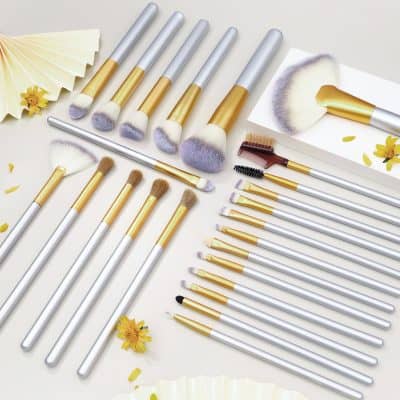 High-quality makeup brushes set with gold and silver handles, perfect for professional and everyday beauty routines, displayed on a white surface with decorative flowers.