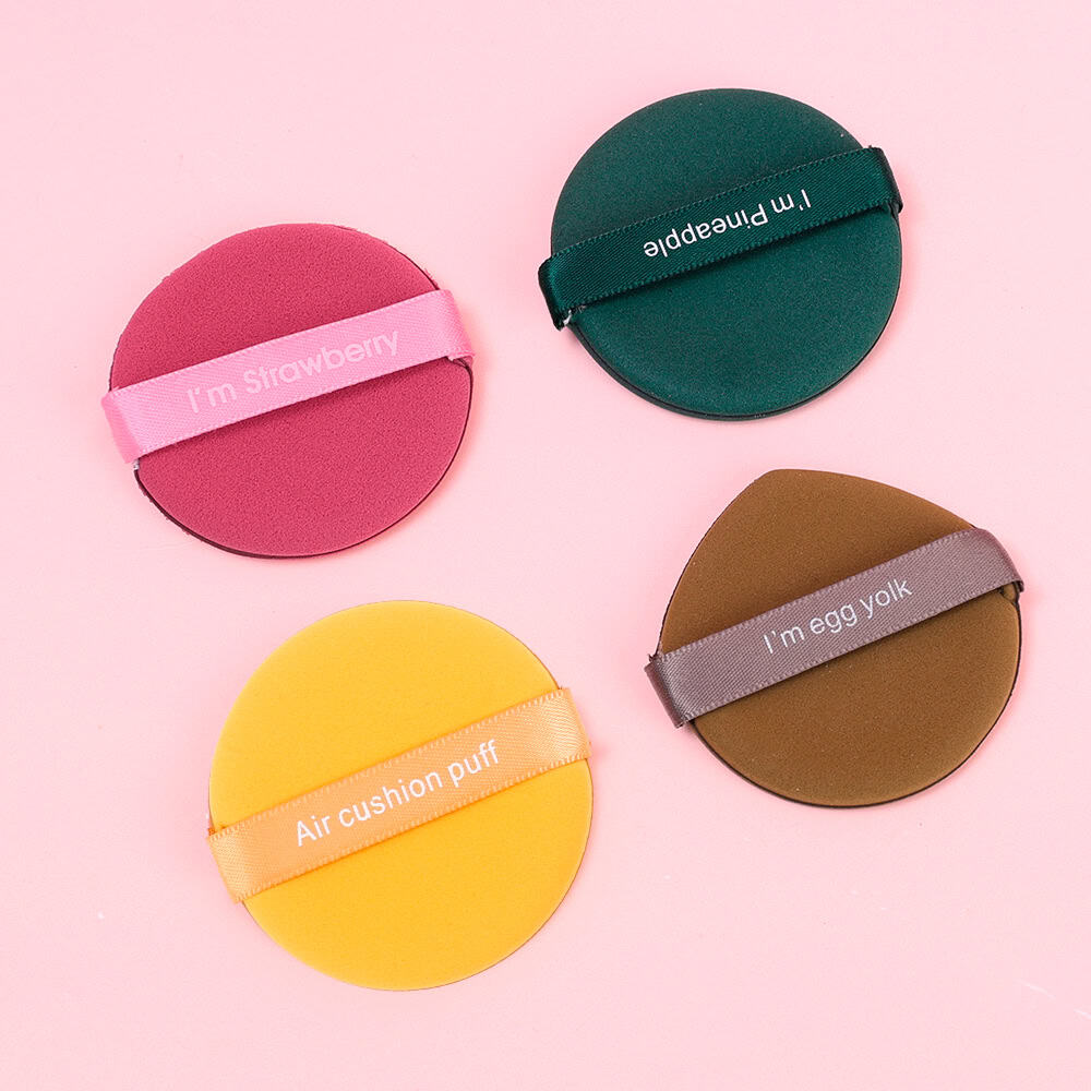 Brightly colored cosmetic sponges with humorous labels for foundation blending, including "I'm Strawberry," "I'm Pineapple," "Air Cushion Puff," and "I'm Egg Yolk" on a pink background.