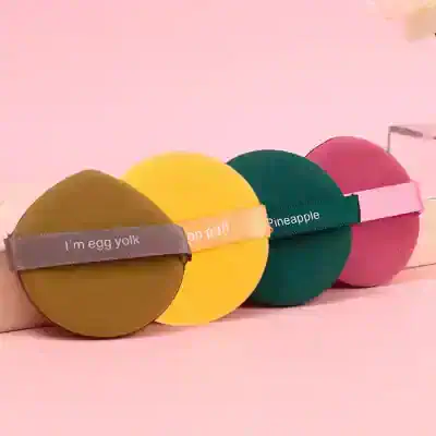 Colorful round makeup sponges with humorous text and vibrant colors, ideal for beauty enthusiasts and professional cosmetic application, displayed on a pink background.