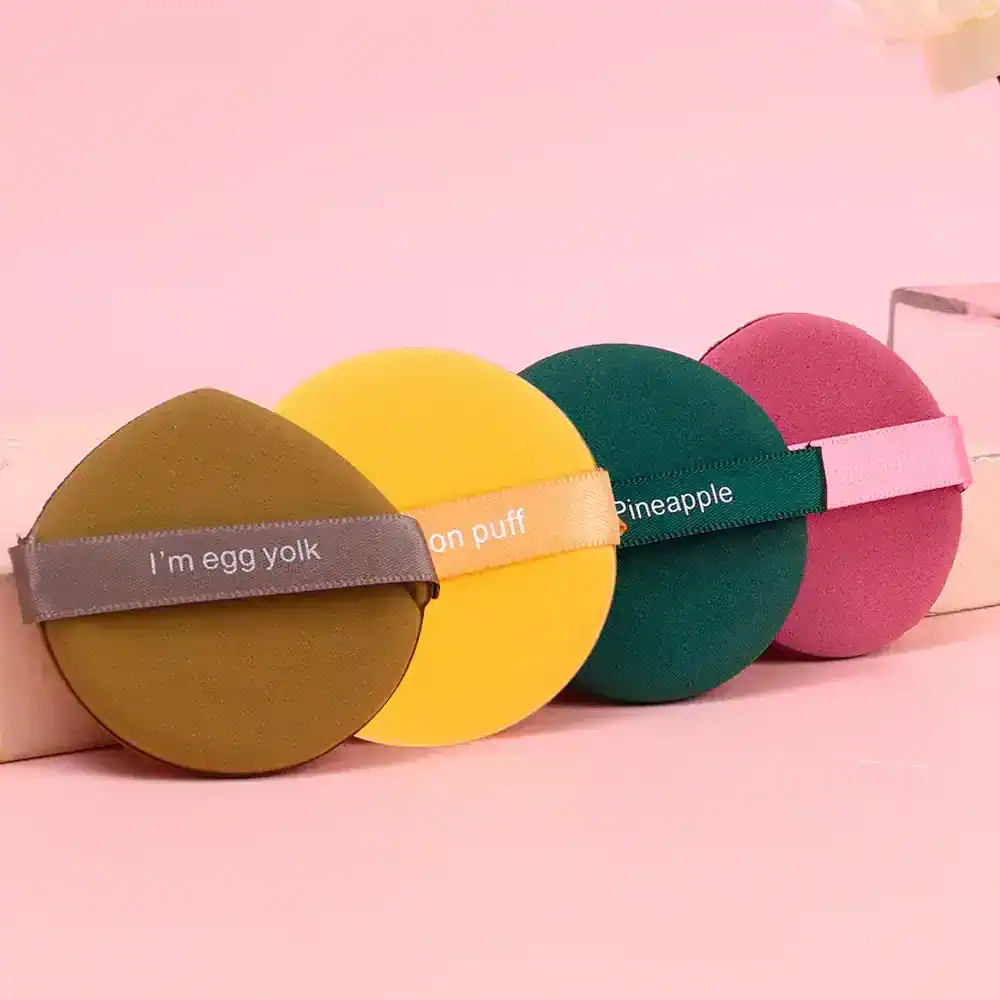 Colorful round makeup sponges with humorous text and vibrant colors, ideal for beauty enthusiasts and professional cosmetic application, displayed on a pink background.