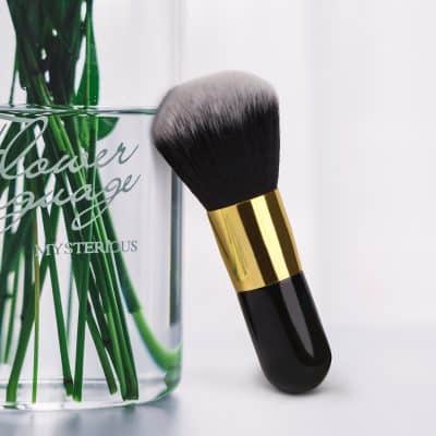 Flawless makeup brush leaning against a glass vase with green flowers, showcasing beauty and cosmetic tools at Monalisa Medical Store.