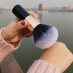 Luxurious makeup brush being held outdoors near a river, showcasing beauty and cosmetics products for skincare and makeup application.