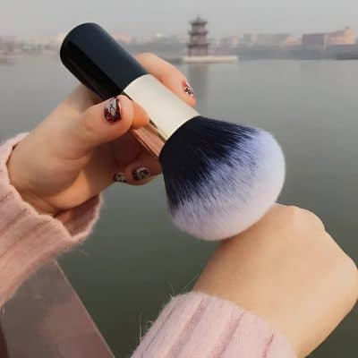 Vegan makeup brush with ombre bristles against a scenic lake background, perfect for professional and home beauty application.