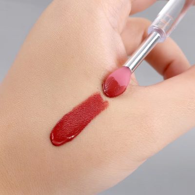 Vibrant red lipstick being applied with a lip brush on a hand, showcasing bold makeup colors.