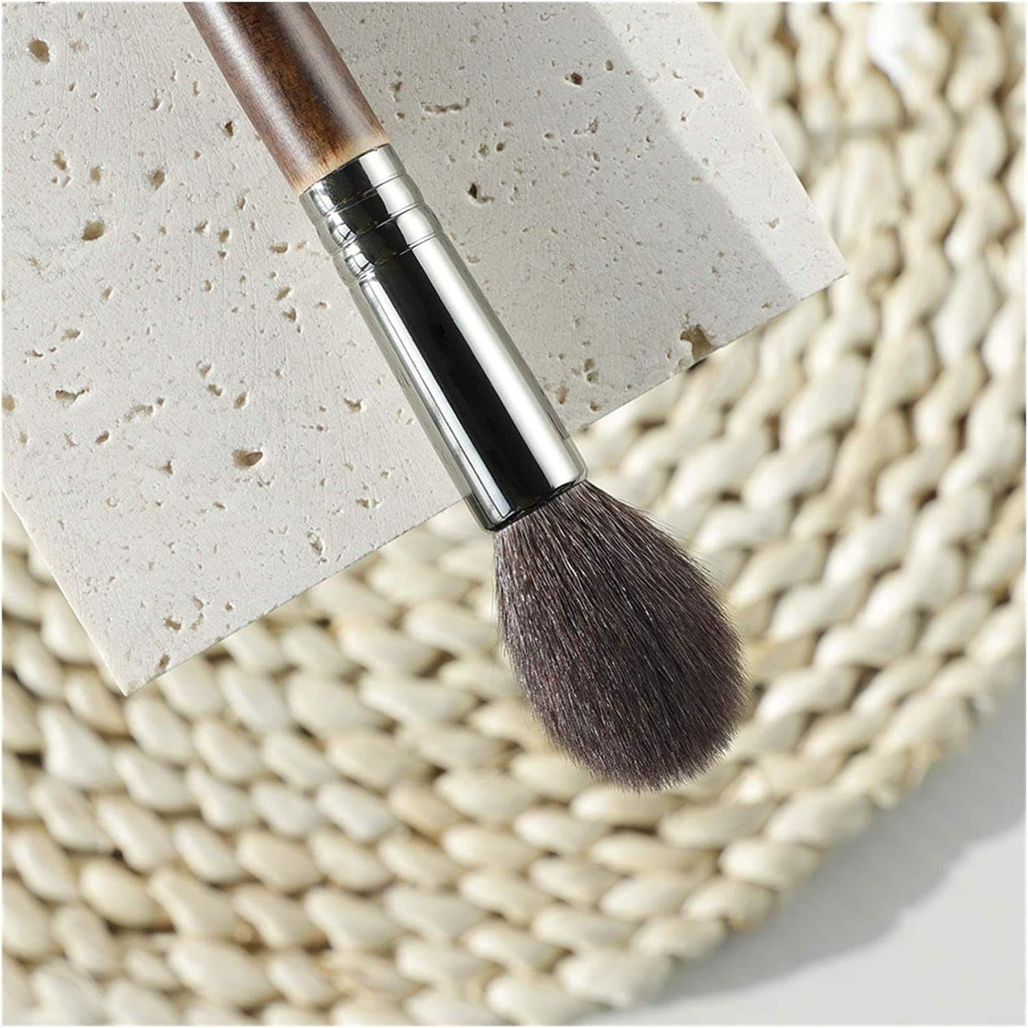 Soft makeup brush with wooden handle, ideal for blending powders and applying foundation, displayed on textured white surface. Perfect for professional and everyday beauty routines.