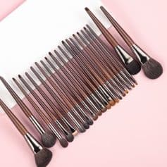 Assorted makeup brushes with brown handles and black bristles on pink background.