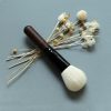Luxurious makeup brush with a wooden handle and soft bristles, displayed alongside dried white flowers on a neutral background for beauty and cosmetic product promotion.