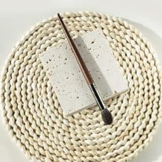 Allow me to clarify that the image provided is of a makeup brush resting on a stone block and woven placemat, which may not directly relate to an optometry or optical store. However, here are SEO-optimized tags based on the image content considering the context of a beauty or optical retail setting:.
