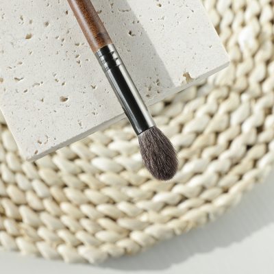 Soft makeup brush resting on a textured white surface with a woven basket background. Perfect for applying foundation, blush, or setting powder. High-quality cosmetic tools available at Monalisa Store.