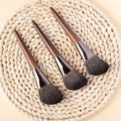 Soft-bristled makeup brushes with wooden handles on a woven round mat, beauty tools for professional cosmetic application.