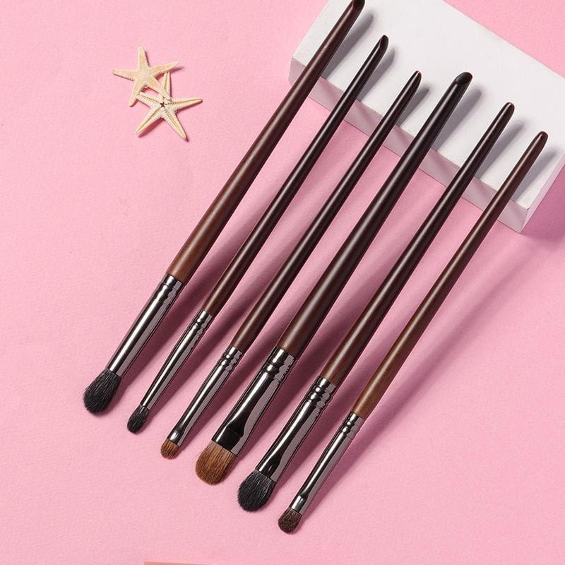 Professional makeup brushes set with brown handles on pink background, perfect for beauty and cosmetics application.