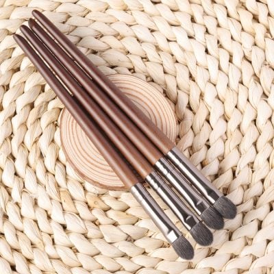Soft-bristle makeup brushes with wooden handles on a woven straw background.