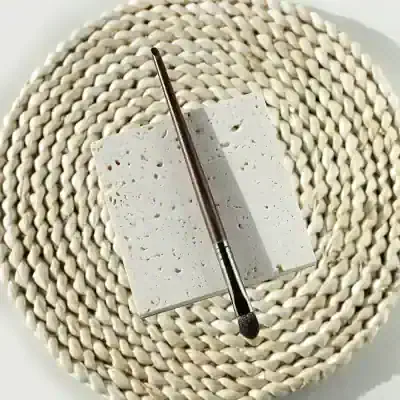 Cosmetic brush on textured white tile and woven placemat, close-up image for beauty and skincare products SEO.