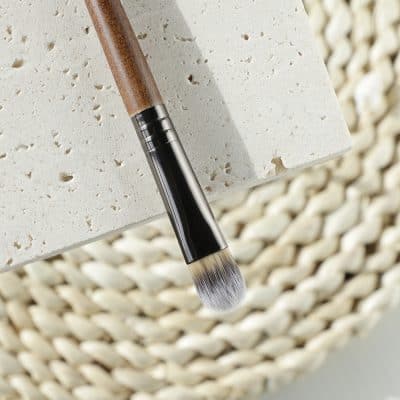 Elegant makeup brush with wooden handle and soft synthetic bristles, perfect for flawless beauty application, displayed on natural textured background.