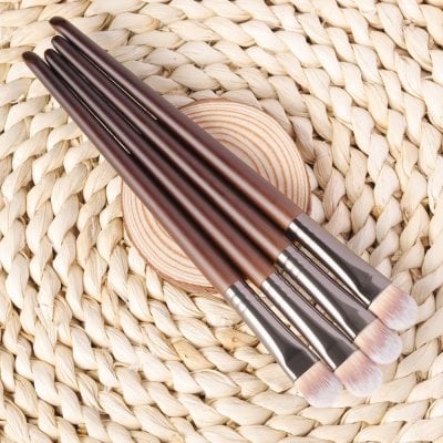 Soft-bristle makeup brushes with wooden handles on woven straw background for skincare or beauty application.