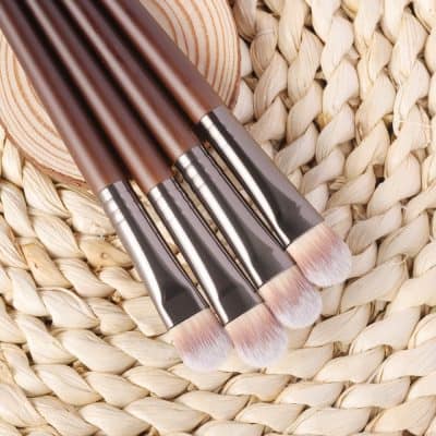 Professional makeup brushes with wooden handles on woven straw background, perfect for beauty and cosmetic application.