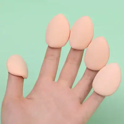 Soft makeup sponge blenders for foundation and cosmetic application, shown on a human finger, ideal for blending beauty products, on a pastel green background.