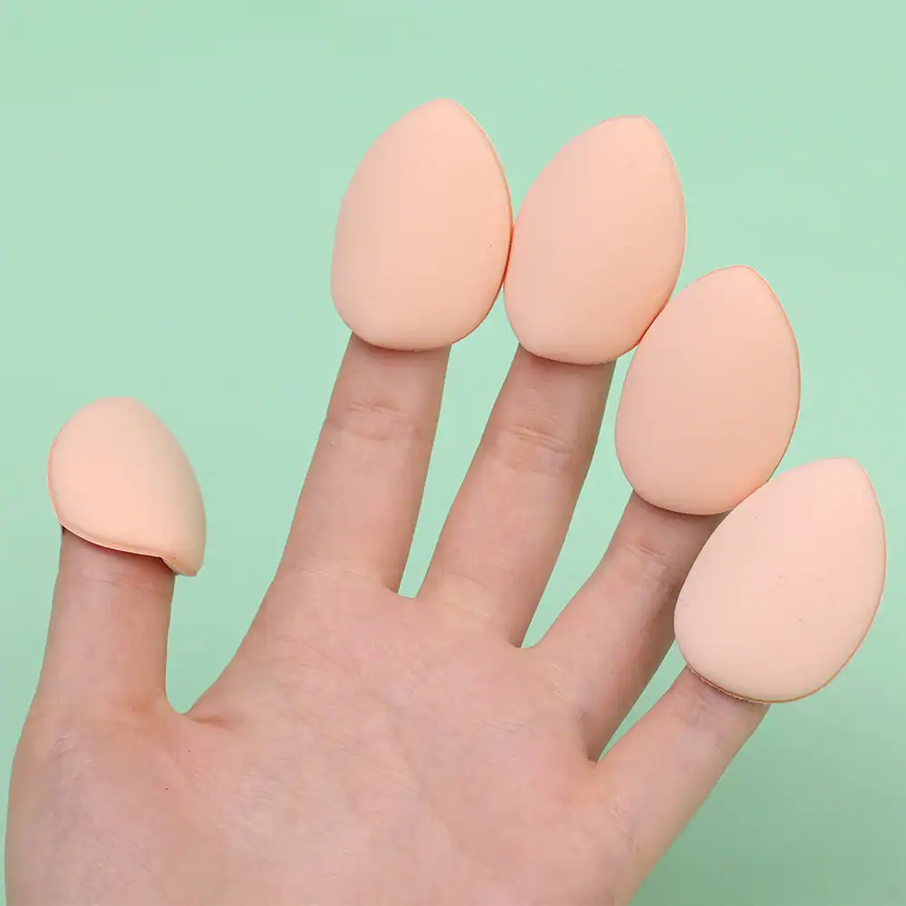 Soft makeup sponge blenders for foundation and cosmetic application, shown on a human finger, ideal for blending beauty products, on a pastel green background.