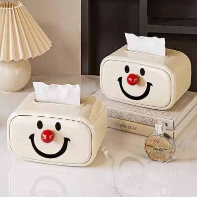 Smile face tissue box holder, decorative napkin dispenser, playful home accessory, novelty tissue box cover with red nose, ideal for living room decor and gift idea for kids' rooms.