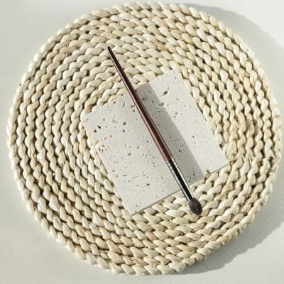 Natural stone sample with makeup brush on woven placemat for beauty and skincare aesthetic.
