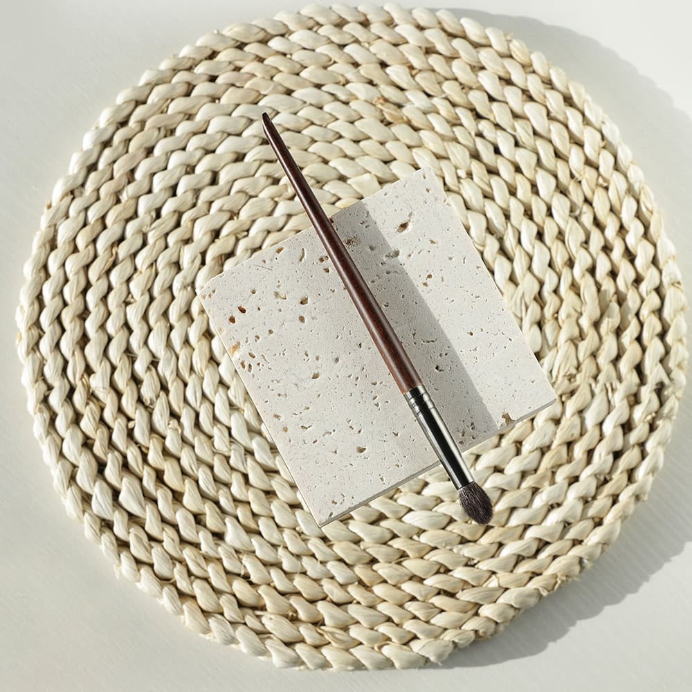 Natural stone sample with makeup brush on woven placemat for beauty and skincare aesthetic.