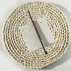 Luxurious beige woven placemat with a white porous ceramic tile and a brown makeup brush on top, perfect for beauty and skincare product display at Monalisa Store.