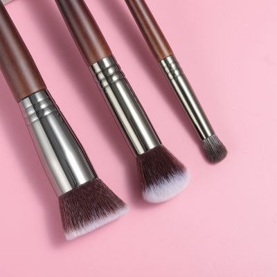 Soft makeup brushes with wooden handles and metallic accents on a pink background for professional beauty application.