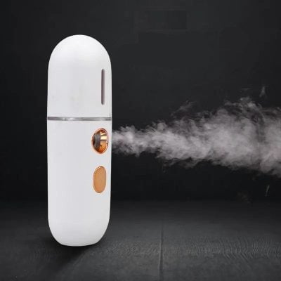 Aesthetic handheld disinfectant spray device emitting mist, modern design, for skincare and personal hygiene. Perfect for at-home or professional use, featuring sleek white and gold accents.