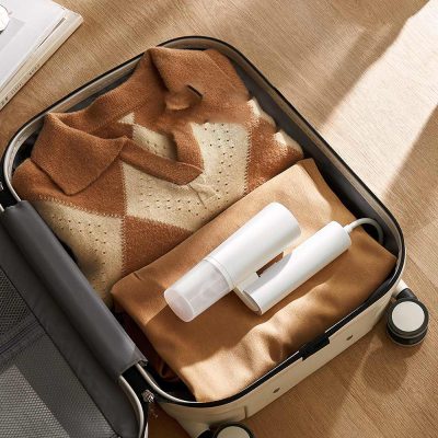 Folded beige and brown argyle sweater inside a carry-on suitcase with portable steamer and clothes at Monalisa Medical store.