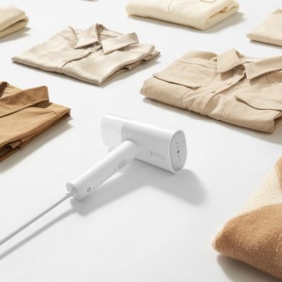 Gentle laundry sterilizer device with temperature control on a white table with folded clothes in neutral tones, emphasizing hygiene and skincare in clothing care.