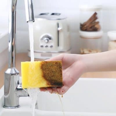 Cleaning a yellow sponge under a running kitchen faucet in a modern kitchen setting.