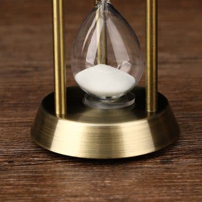 Silicon hourglass with white sand, brass frame, on wooden surface, used for time management and decorative purposes.