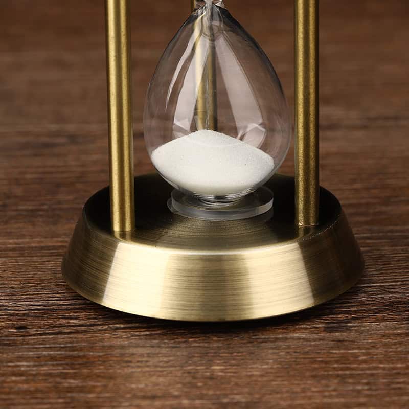 Silicon hourglass with white sand, brass frame, on wooden surface, used for time management and decorative purposes.