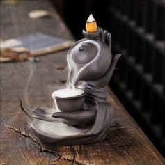 A decorative ceramic teapot with a built-in cup and incense stick holder, gray and black tones, placed on a rustic wooden surface for a cozy, tranquil ambiance.