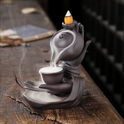 A decorative ceramic teapot with a built-in cup and incense stick holder, gray and black tones, placed on a rustic wooden surface for a cozy, tranquil ambiance.