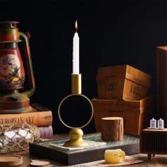 Candle holder with a lit white candle on a wooden table, surrounded by vintage coffee crates, books, and decorative items, creating a cozy, rustic ambiance.