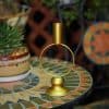 Gold candle holder with circular design on mosaic table near potted succulent plant.