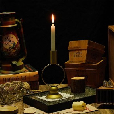 Candlestick with a lit candle on a vintage table surrounded by books and decorative objects, cozy ambient lighting.