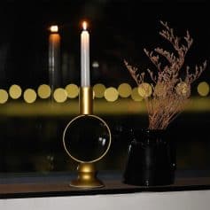 Elegant gold candle holder with a lit white candle and a black vase with dried flowers, perfect for home decor and aesthetic interior design.
