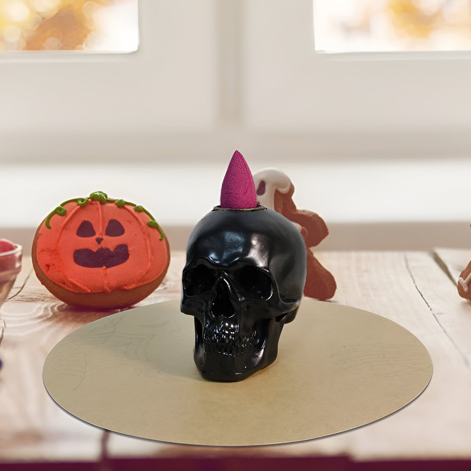 Black skull candle with pink embellishment, surrounded by Halloween pumpkin cookies and gingerbread characters for festive holiday décor.