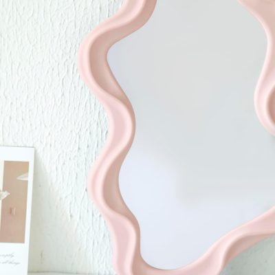 Wave-edged decorative mirror with blush pink frame for modern home décor.