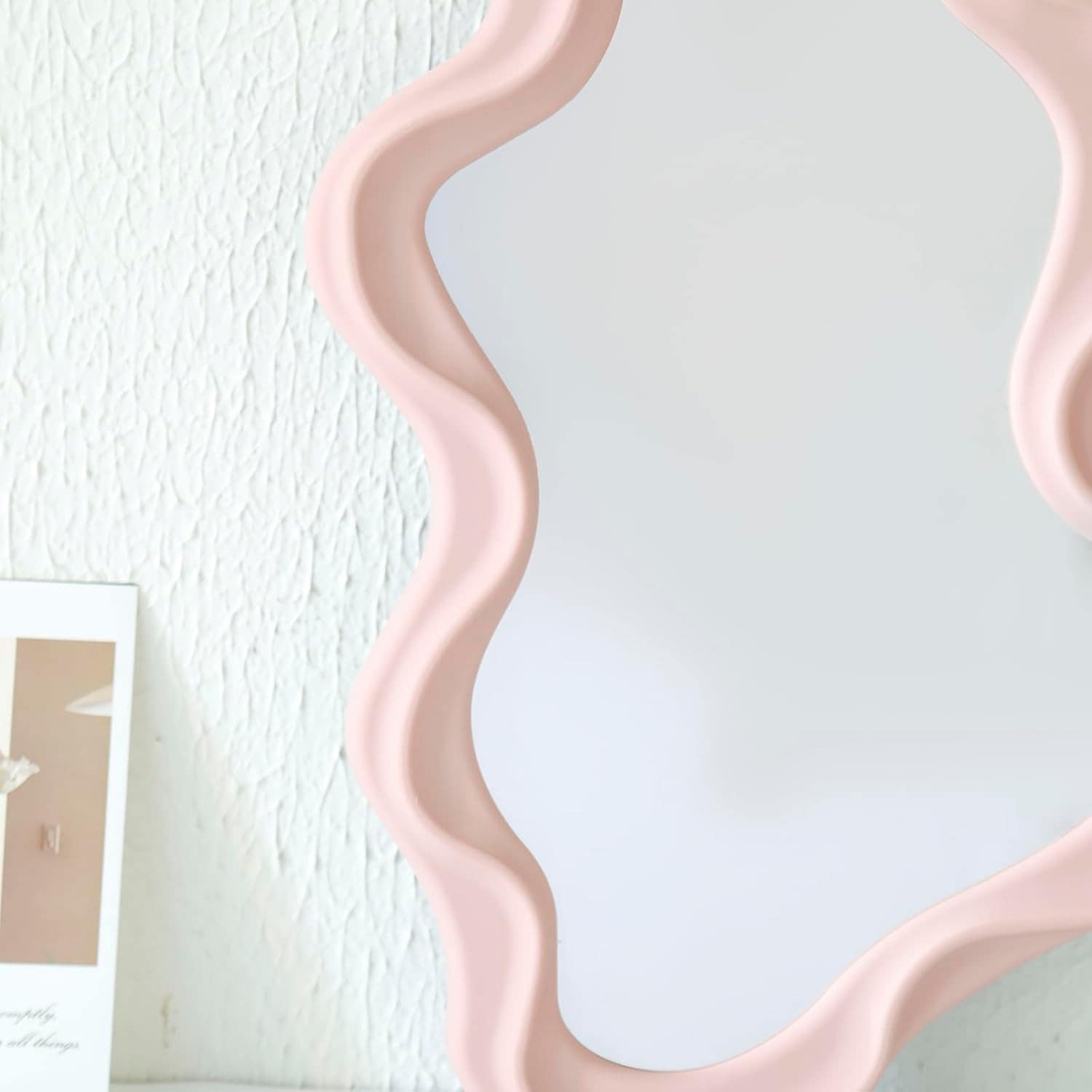 Wave-edged decorative mirror with blush pink frame for modern home décor.