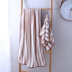 Soft beige and white striped bath towels hanging on a wooden towel rack, perfect for bathroom decor and spa use.