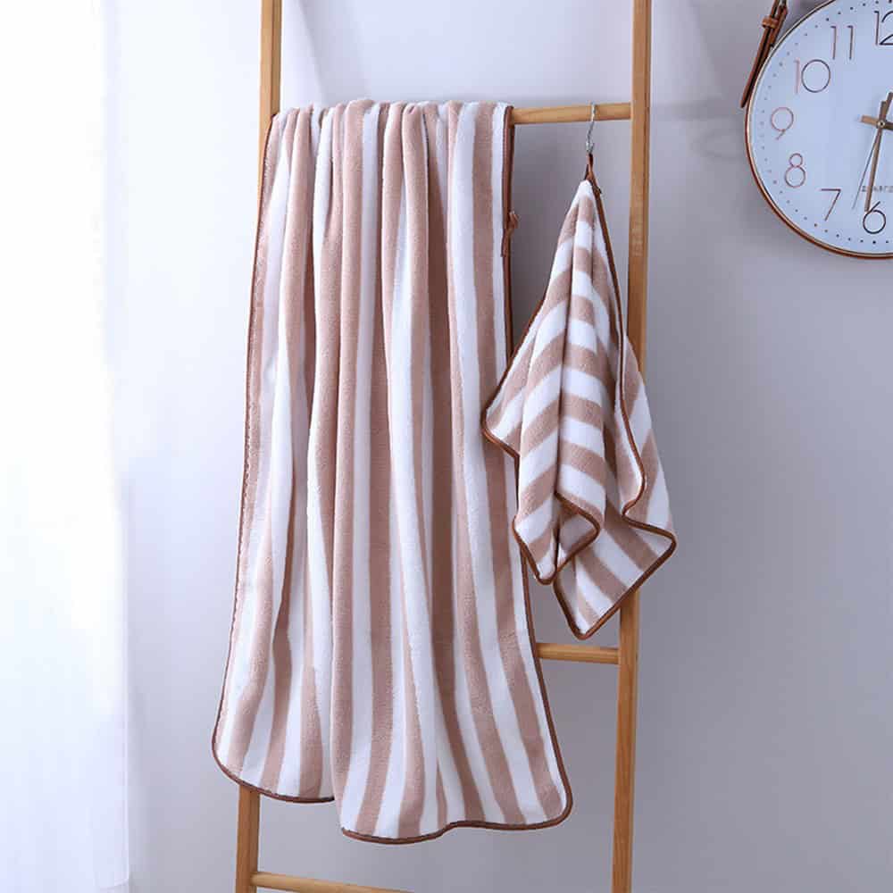 Soft beige and white striped bath towels hanging on a wooden towel rack, perfect for bathroom decor and spa use.