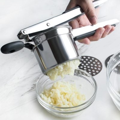 Freshly pressed potatoes being mashed through a stainless steel potato ricer in a modern kitchen setting. Perfect for making smooth mashed potatoes, gnocchi, or other potato-based dishes.