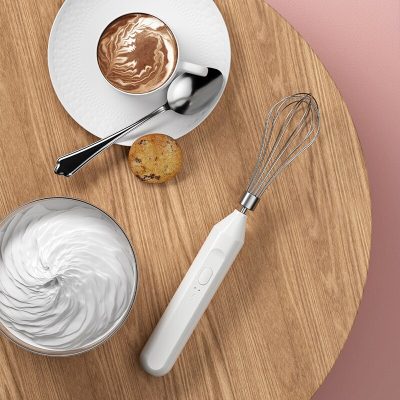Whisk with handheld electric mixer, bowl of whipped cream, chocolate chip cookie, and hot cocoa on wooden table, promoting Monalisa Store's kitchen appliance selection.