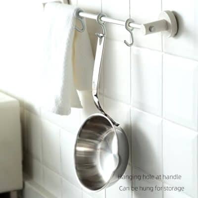 Bright stainless steel saucepan hanging from wall hook in kitchen or laundry room, with towel nearby, useful for cooking or cleaning.