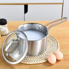 Creamy liquid in stainless steel saucepan with lid on woven placemat, eggs and condiments on wooden table, kitchen cookware with milk, cooking, kitchen utensils, food preparation, Monalisa Store.